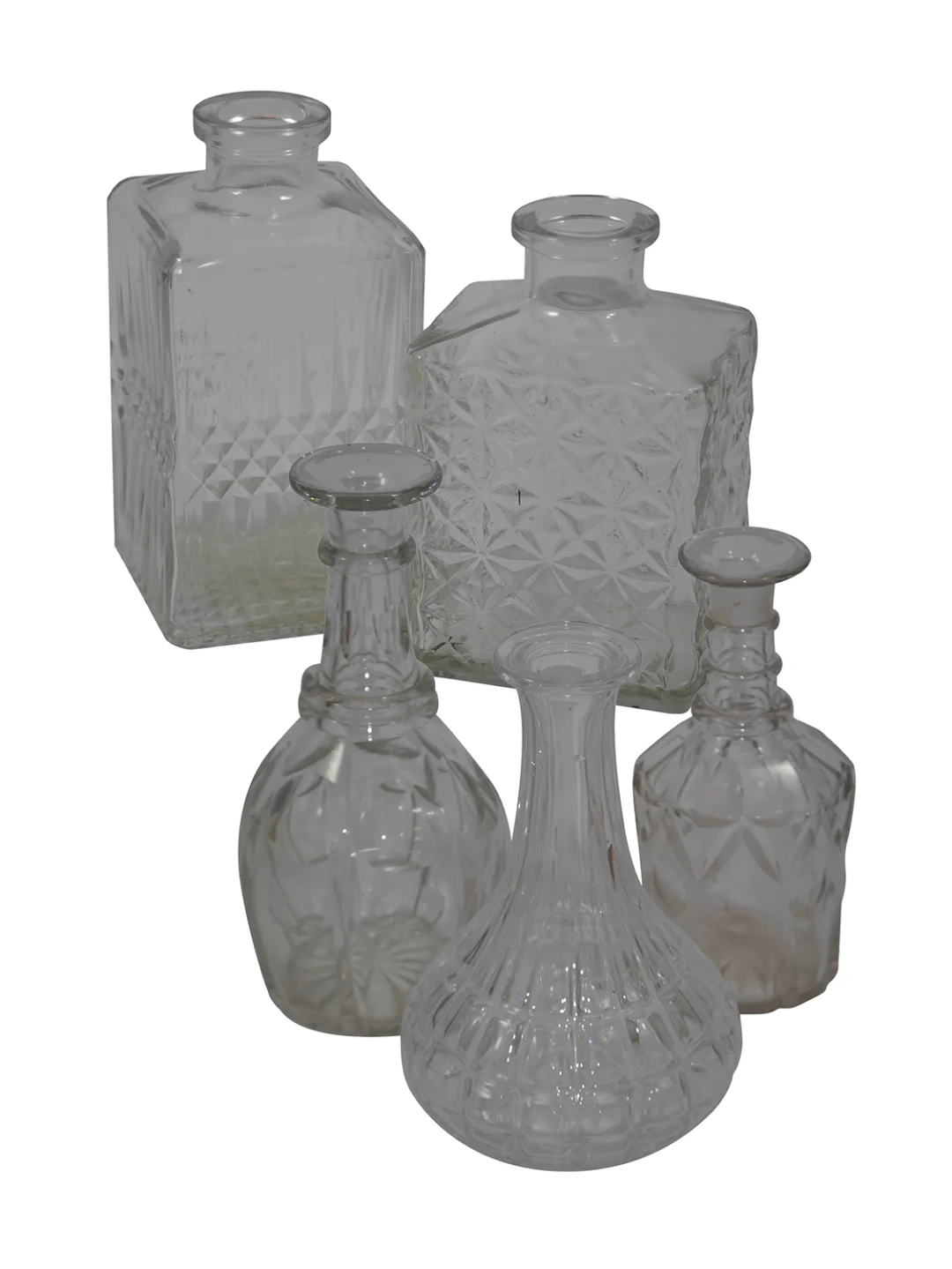 Set of five clear glass bottles and decanters with intricate cut patterns arranged together on a white background.