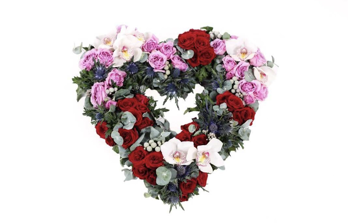 Heart-shaped bouquet made of red, pink, and white flowers with greenery, arranged to form a floral heart.